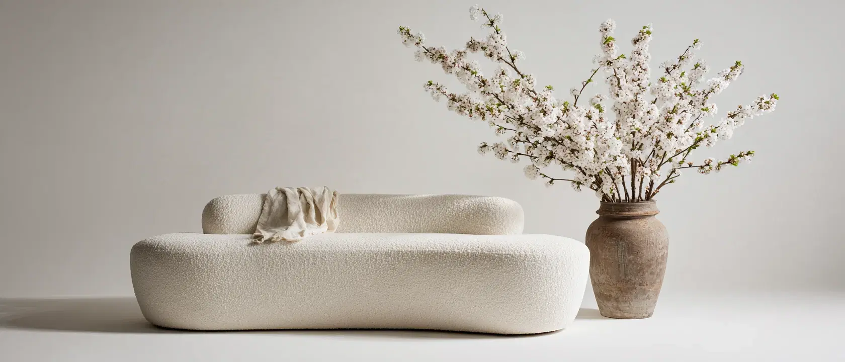 The ivory bouclé sofa, delivered and in place, beside a stoneware urn of white blossom