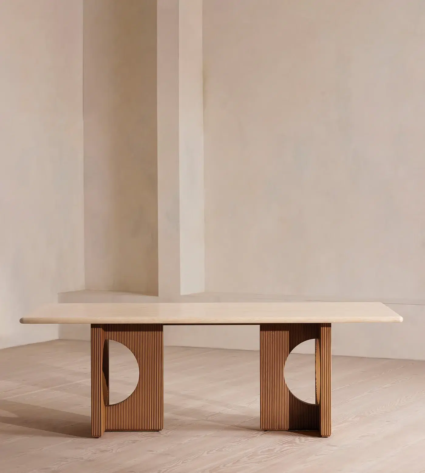 A travertine-topped dining table on sculpted oak legs in a limewashed room